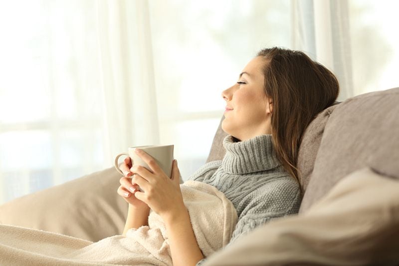 A woman relaxes on a couch with a mug. Zone Control Systems.